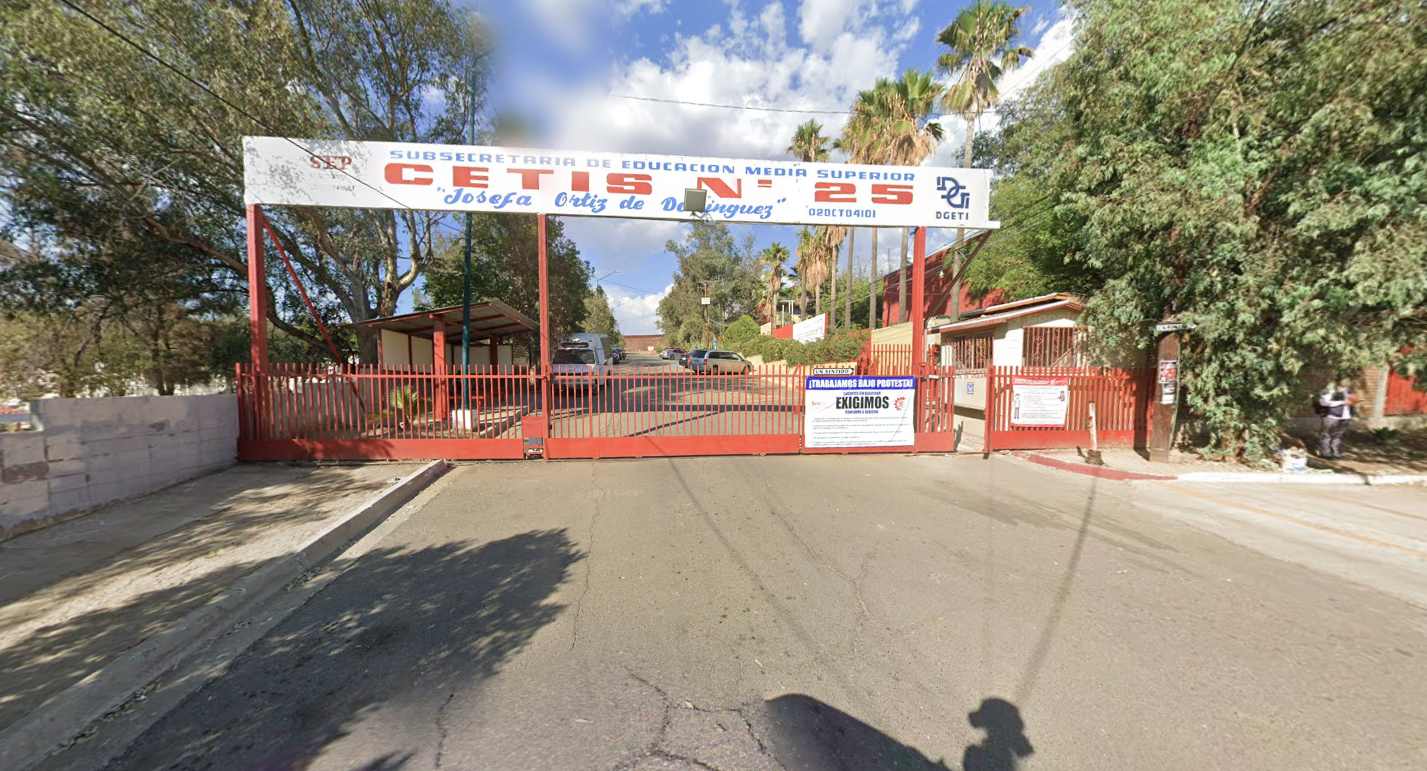 En la fotografía se muestra la entrada al plantel que está conformado por una reja de color rojo, arriba de ella, en letras grandes dice CETIS NÚMERO 25 y al final de la reja del lado derecho se encuentra el acceso al plantel.